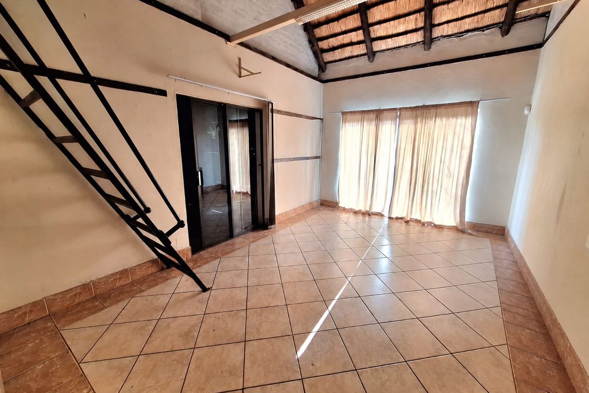Spacious living area featuring high vaulted thatched ceilings, tiled flooring, and a metal staircase leading to an upper level.