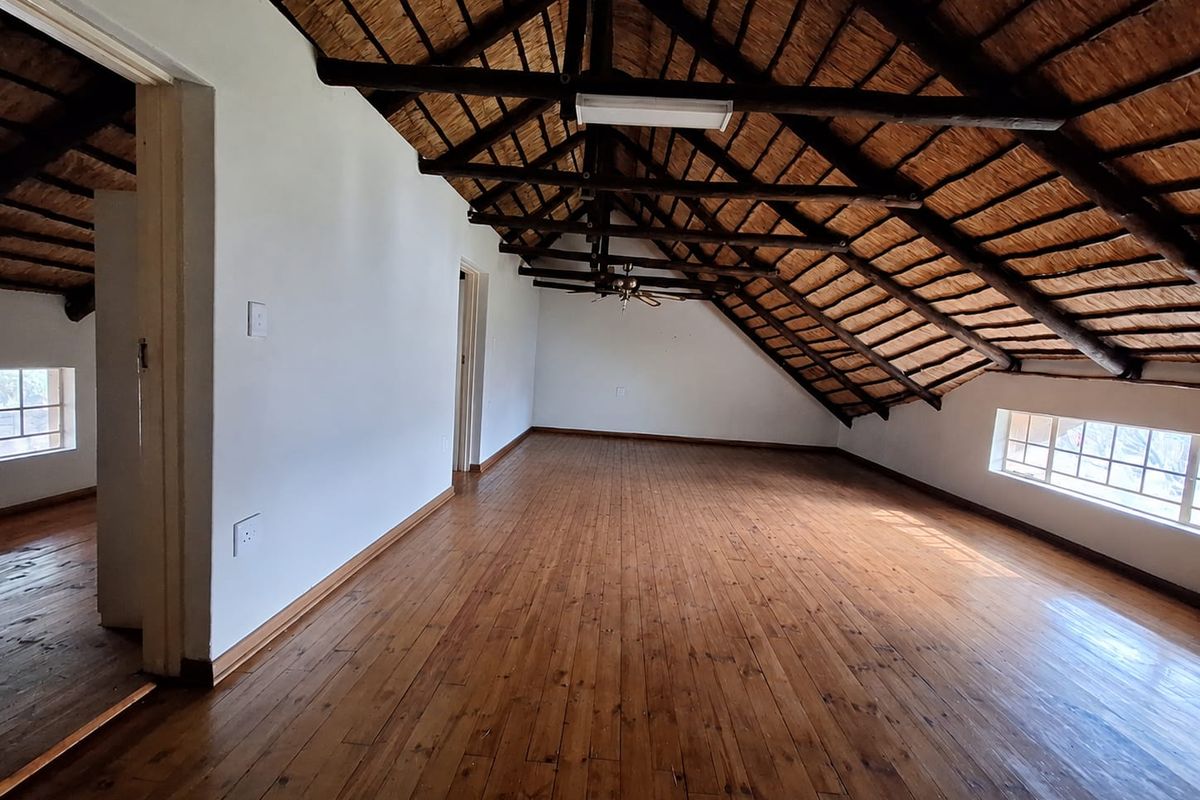 Spacious loft-style bedroom featuring exposed timber roof trusses, a traditional thatched ceiling, and polished wooden flooring with natural light from multiple windows.