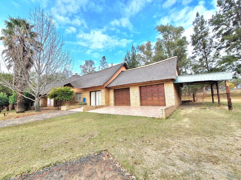 A single-story brick house featuring a traditional thatched roof, double garage, and an attached carport, set on a spacious lawn.