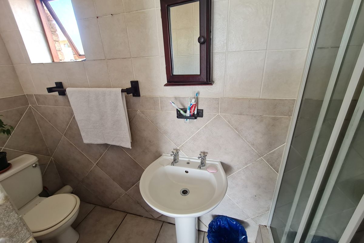 A functional bathroom featuring a pedestal basin, toilet, and shower enclosure with tiled finishes and a wall-mounted medicine cabinet.