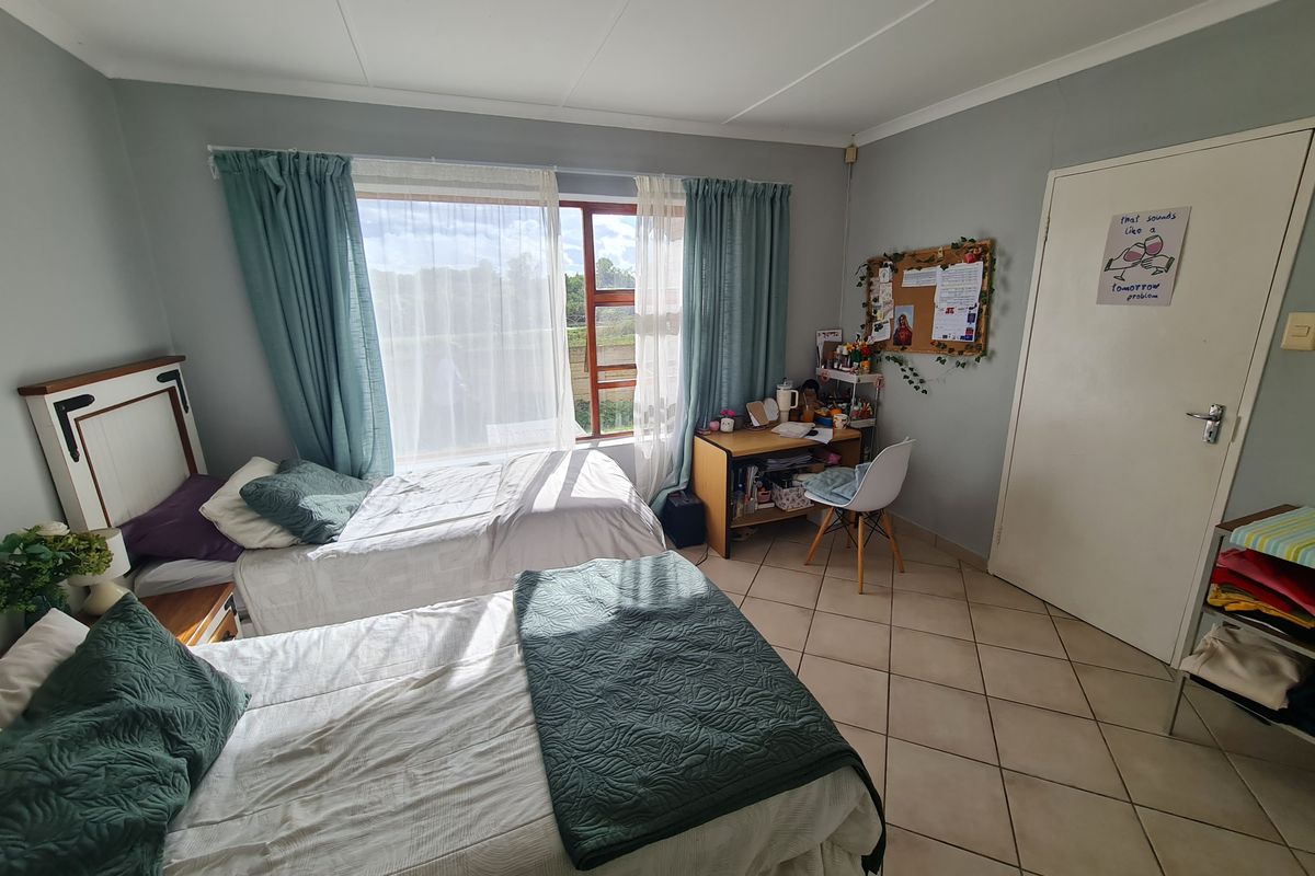 A functional bedroom featuring tiled flooring, a large window allowing natural light, and a standard interior door.