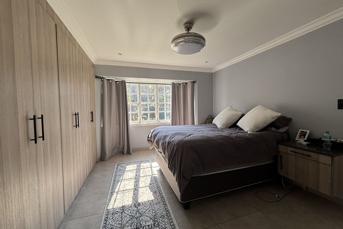 A well-maintained bedroom featuring neutral tiled flooring, extensive built-in wooden cupboards, and a central ceiling fan with integrated lighting.