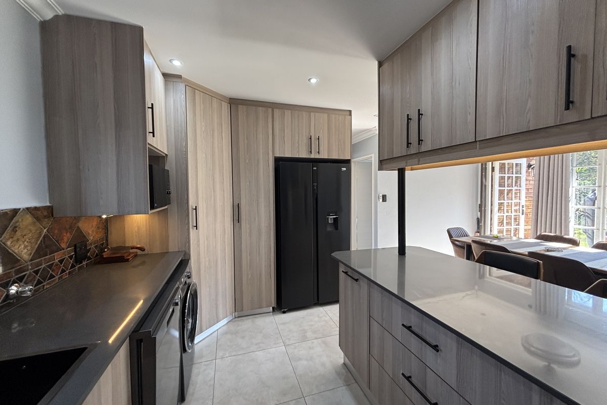 Modern kitchen featuring wood-grain cabinetry, stone countertops, a tiled backsplash, and a functional island, seamlessly connecting to the adjacent dining area.