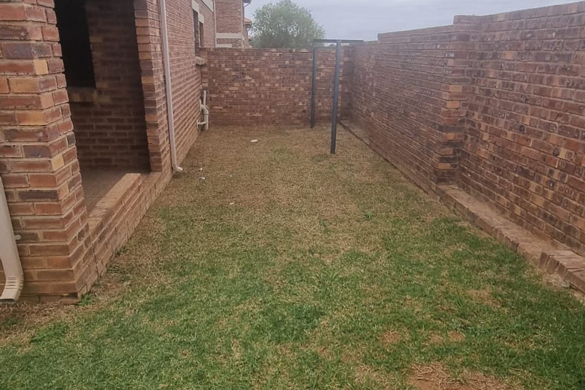 A private rear garden area featuring a brick-walled perimeter and a covered patio section, offering a blank canvas for outdoor landscaping.