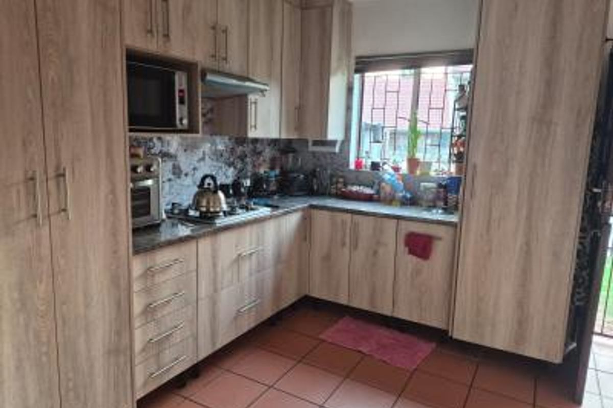 A functional kitchen featuring wood-look laminate cabinetry, granite countertops, built-in appliances including an oven and gas hob, and durable tiled flooring.