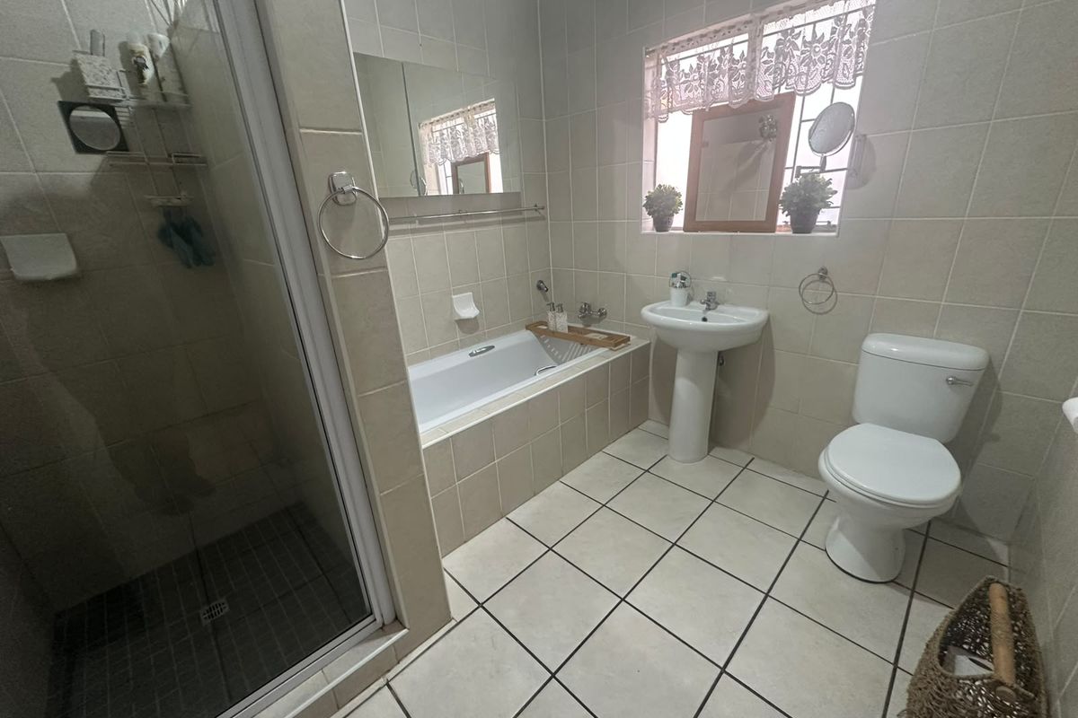 A functional bathroom featuring a separate shower enclosure, a built-in bathtub, a pedestal basin, and a toilet with neutral wall and floor tiling.