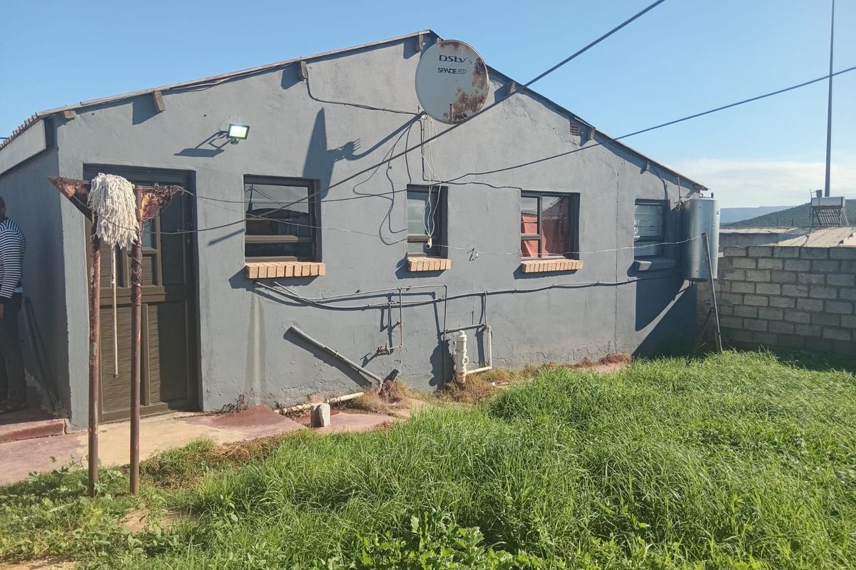 Rear exterior view of the house featuring grey painted walls, external plumbing, a satellite dish, and a small garden area.