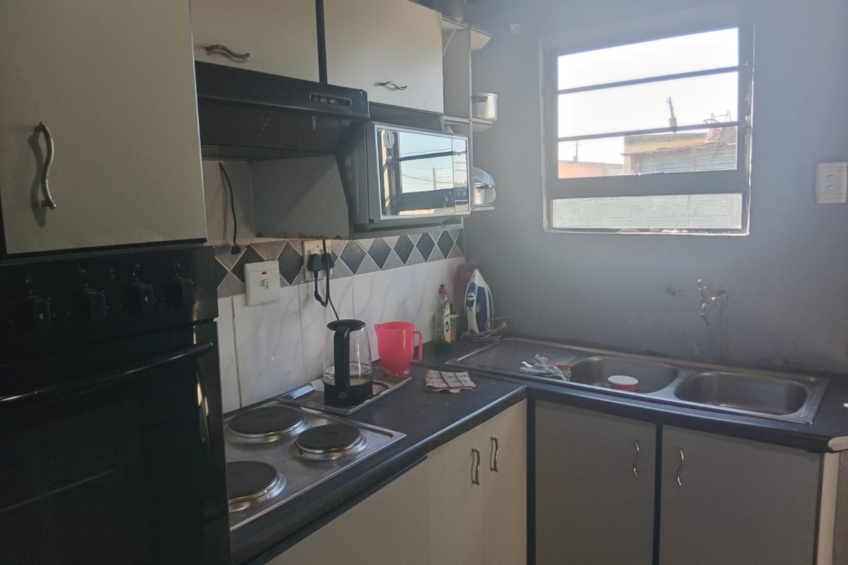 A functional kitchen featuring built-in cabinetry, an electric hob, an integrated oven, and a double bowl sink with a tiled splashback.