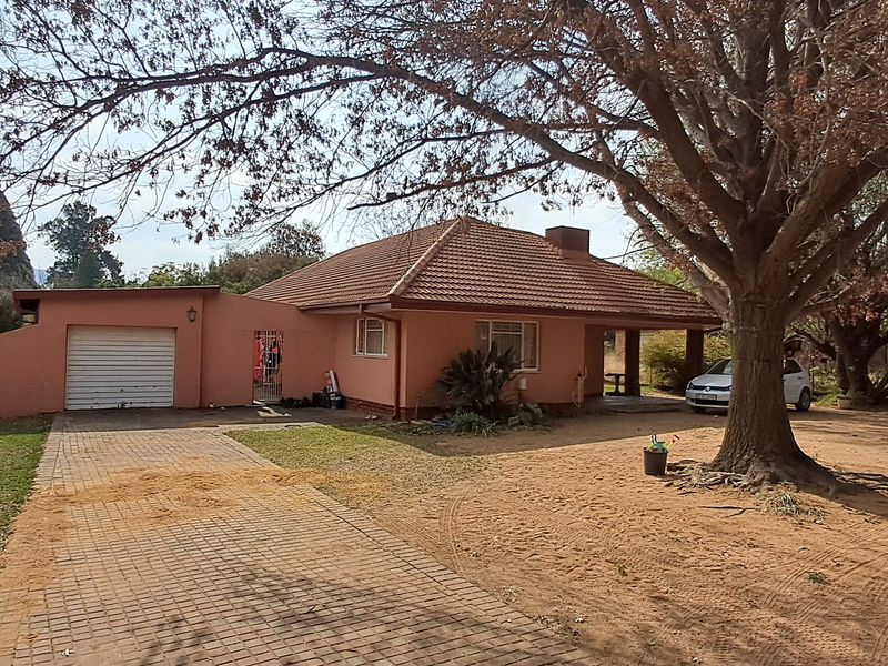 Front view of a single-story house featuring a tiled roof, paved driveway, and an attached single garage set on a large plot.