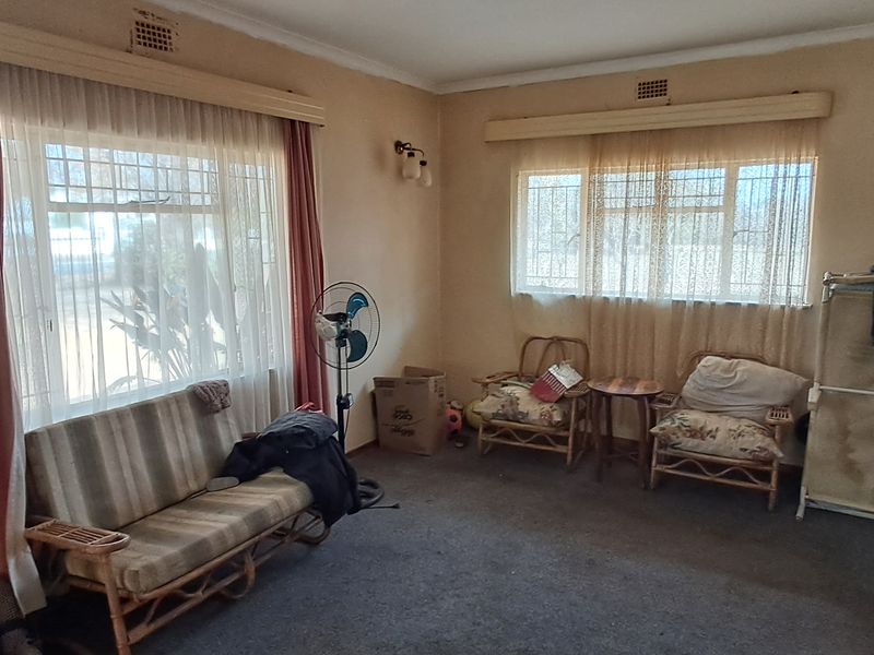 A living room featuring steel-framed windows, carpeted flooring, and coved ceilings, requiring cosmetic updates to improve its overall appeal and condition.