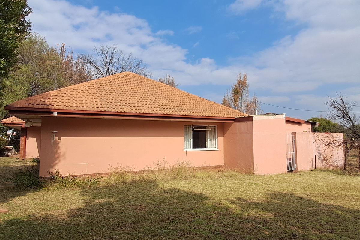 Rear view of the property featuring a tiled roof, plastered exterior walls, and a large garden area requiring maintenance.