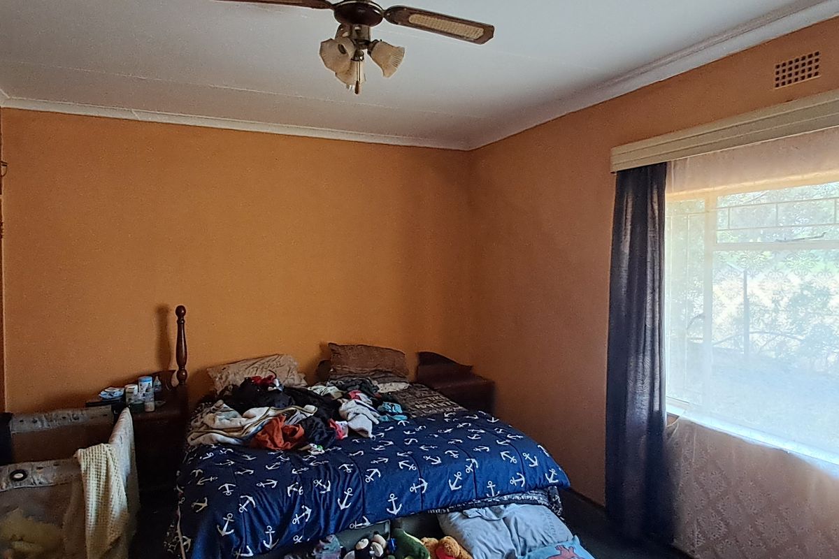 A bedroom featuring built-in cupboards, a ceiling fan, and security bars on the window, offering a functional space ready for cosmetic updates.