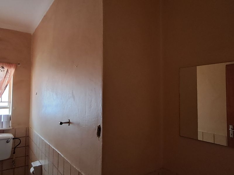 A dated bathroom featuring a toilet cistern, wall-mounted mirror, and tiled splashback, requiring cosmetic updates to improve its overall condition and appeal.