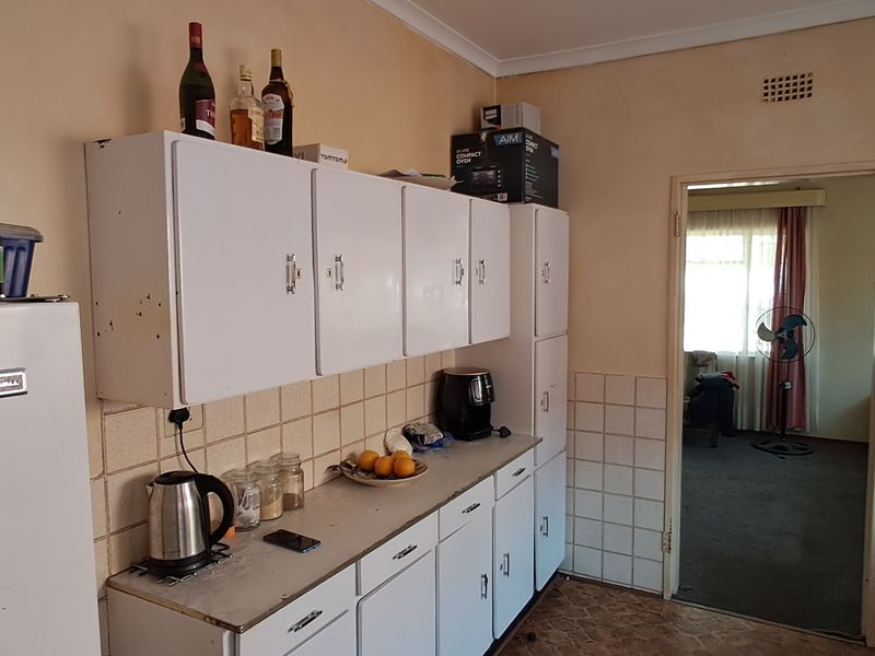A dated kitchen featuring white built-in cabinetry, tiled splashbacks, and laminate countertops, with a doorway leading to an adjacent living area.