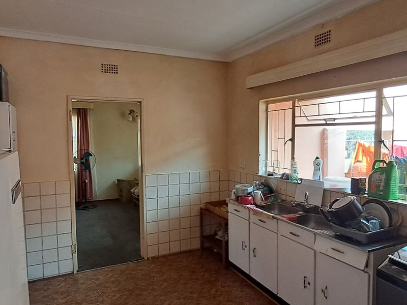 A dated kitchen featuring original cabinetry, a double basin sink, and tiled splashbacks, offering significant potential for a modern renovation.