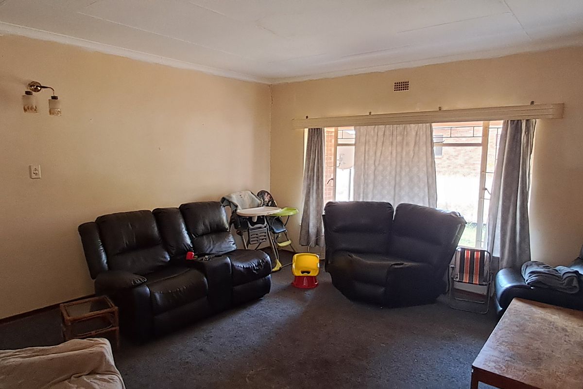 Spacious living room featuring a brick fireplace, large window for natural light, and carpeted flooring, offering a blank canvas for renovation.