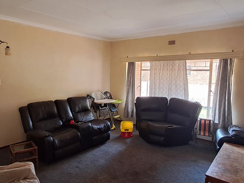 A spacious living room featuring a brick fireplace, wall-mounted lighting, and large windows, offering a blank canvas for potential renovation and modernization.