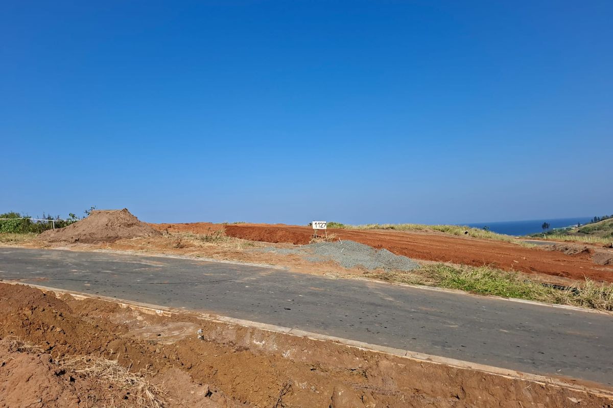 A vacant residential plot featuring a paved road frontage and clear views of the surrounding landscape and coastline.