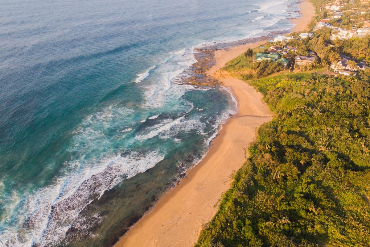 An aerial view of the coastal landscape, showcasing the sandy beach, ocean waves, and surrounding natural vegetation.