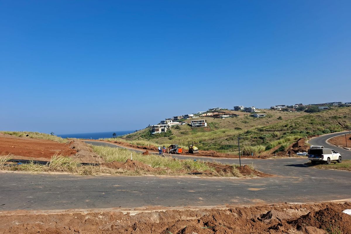 A view of a residential vacant land development site featuring paved roads and ongoing infrastructure work with coastal hillside views.