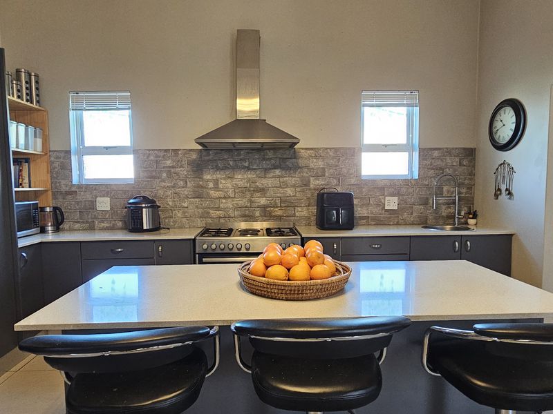Modern kitchen featuring a central island with stone countertops, gas hob, stainless steel extractor fan, and ample built-in cabinetry with a tiled backsplash.