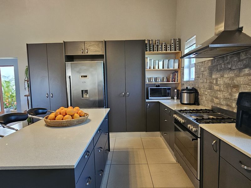 Modern kitchen featuring dark cabinetry, stone countertops, a central island, and a stone veneer backsplash, complemented by stainless steel appliances and tiled flooring.