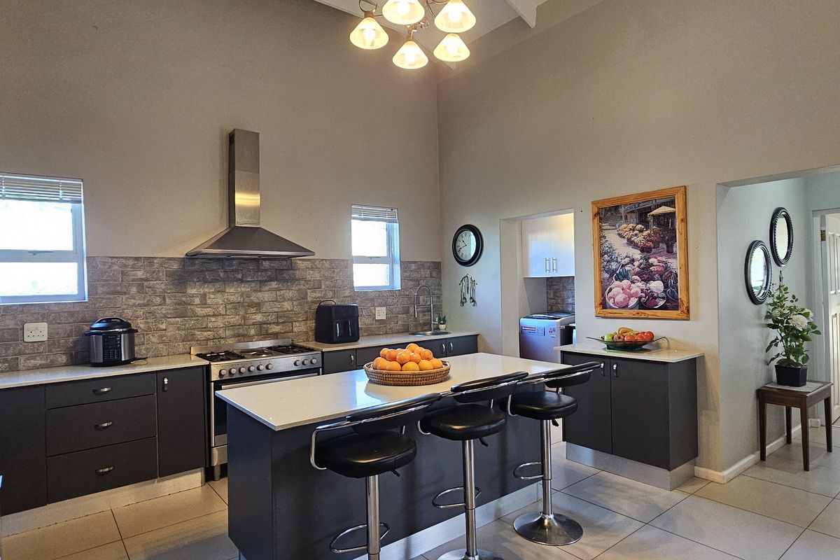 Modern kitchen featuring a central island with stone countertops, dark cabinetry, stainless steel appliances, and a high vaulted ceiling with tiled flooring.