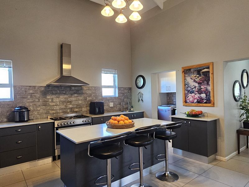 Modern kitchen featuring a central island with stone countertops, dark cabinetry, stainless steel appliances, and a high vaulted ceiling with tiled flooring.