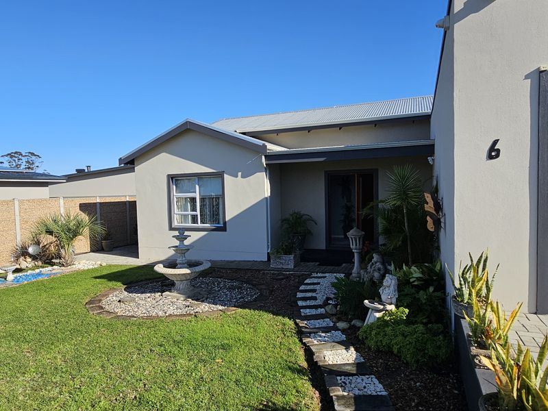 Front view of the property featuring a landscaped garden, stone pathway, water fountain, and a paved driveway leading to the garage.