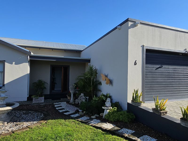 Front elevation of a modern house featuring a paved driveway, single garage, and a landscaped garden with a stone water feature.