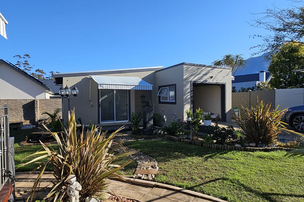 A well-maintained rear garden area featuring a paved walkway, a sliding glass door with a retractable awning, and an attached garage.