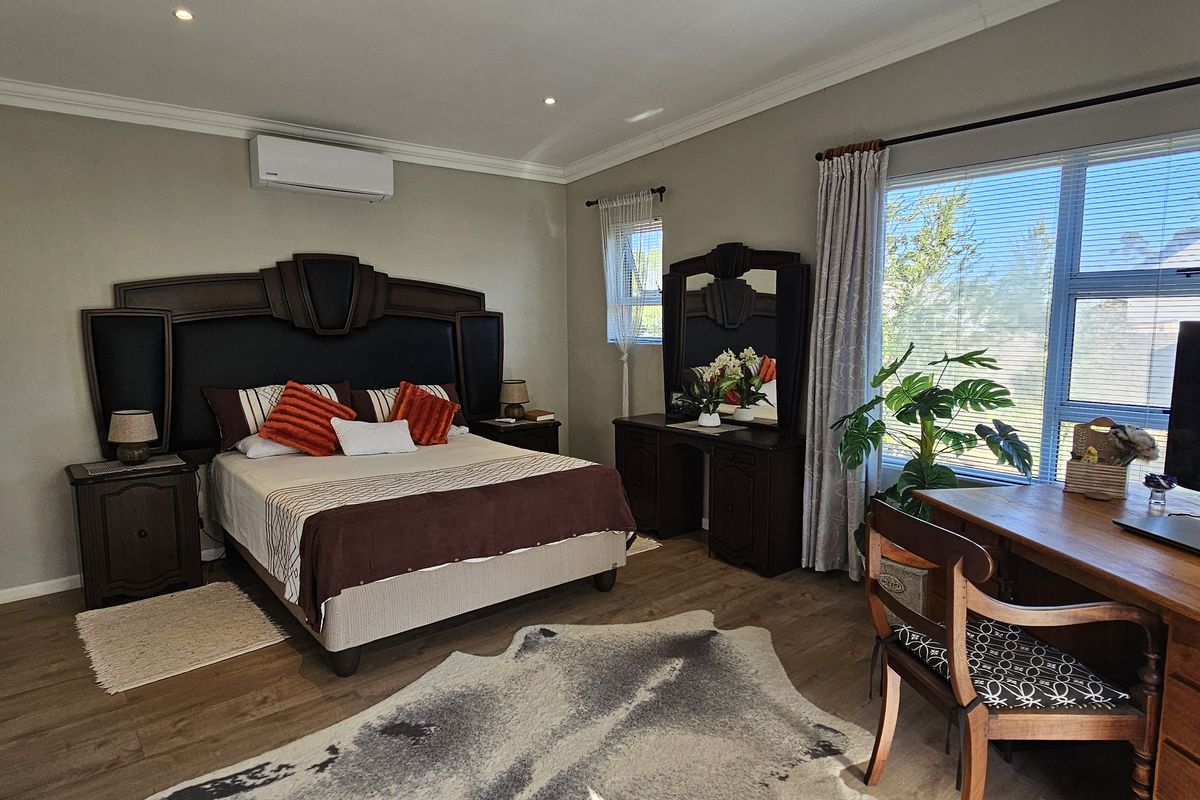 Spacious bedroom featuring laminate flooring, built-in cupboards, recessed downlighting, and a wall-mounted air conditioning unit.