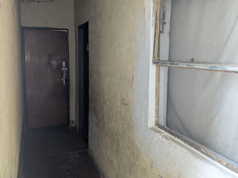 A narrow, empty hallway featuring worn wall finishes and dated timber door and window frames, requiring significant cosmetic refurbishment.