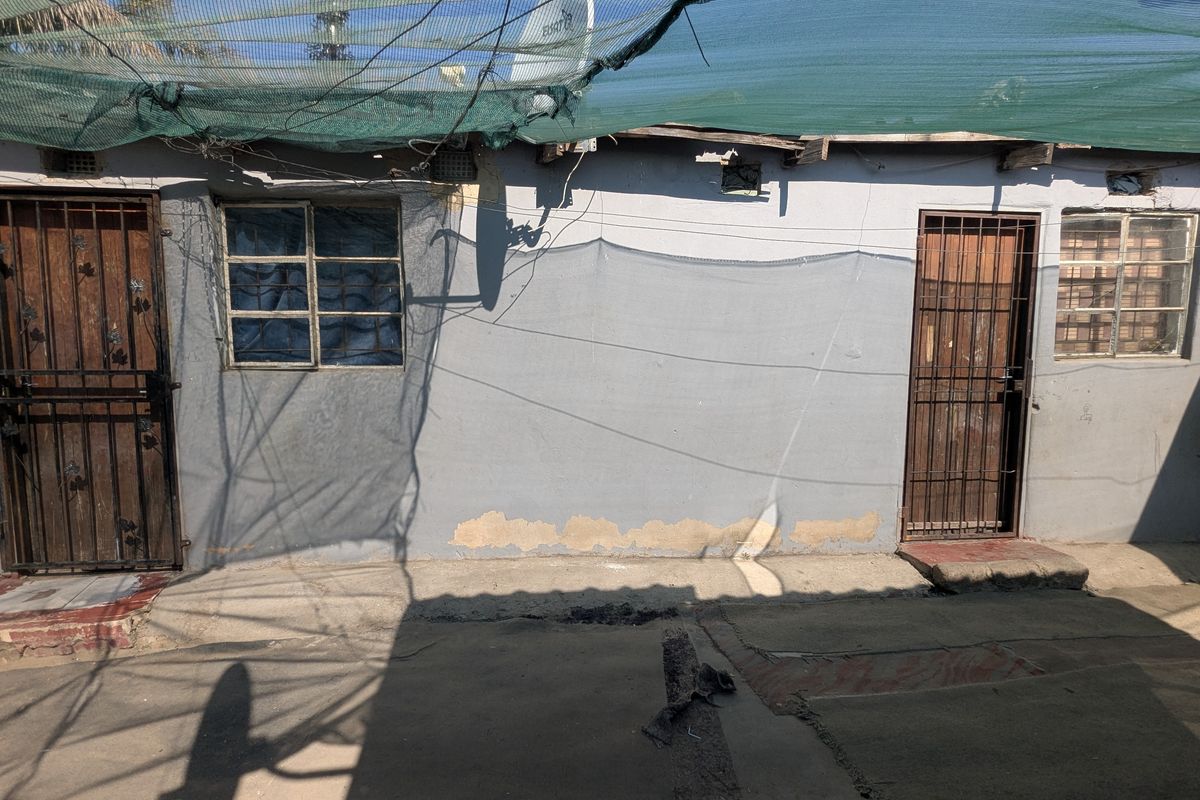 Rear exterior view of the property featuring security gates, steel window frames, and concrete paving, showing signs of wear and maintenance requirements.