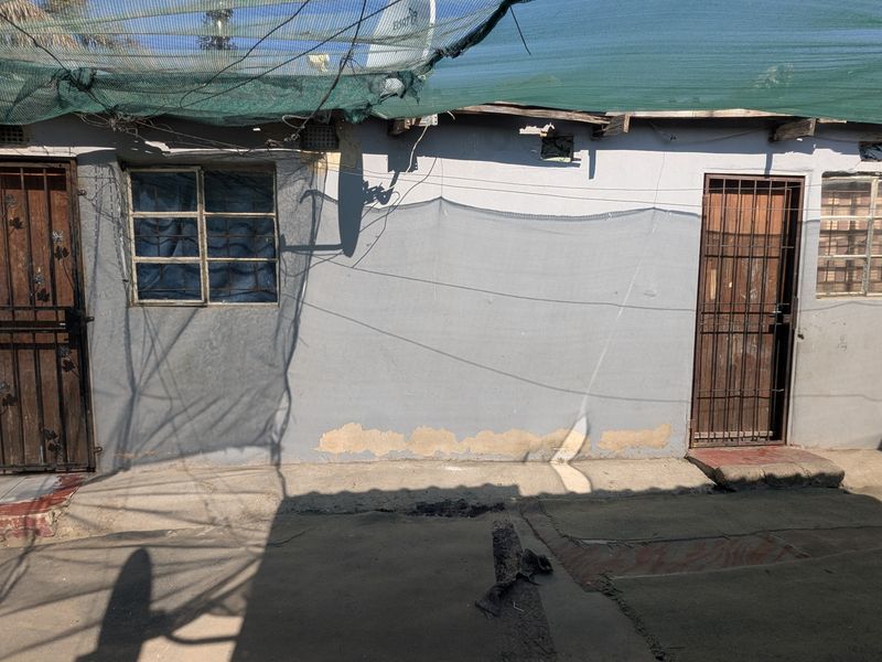 Rear exterior view of the property featuring security gates, steel window frames, and concrete paving, showing signs of wear and maintenance requirements.
