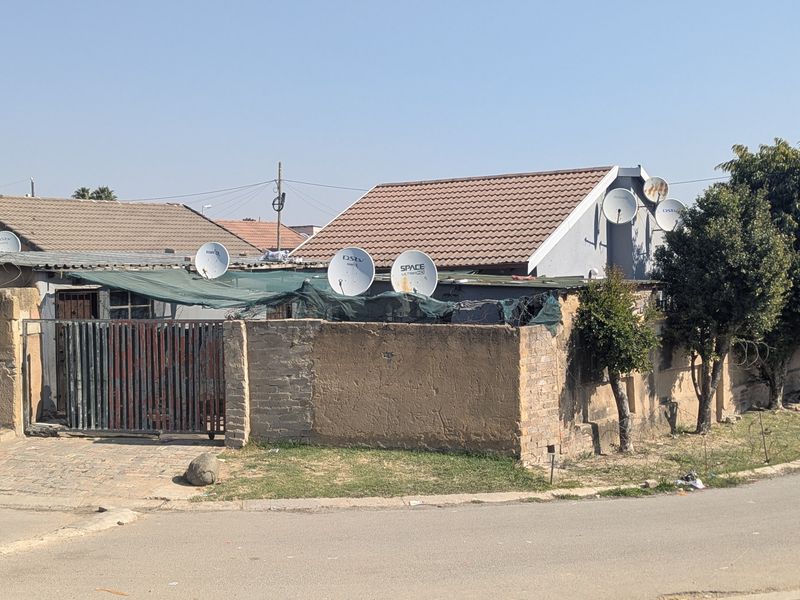 Front exterior view of a residential property featuring a brick boundary wall, metal gate, and tiled roof structure with multiple satellite dishes.