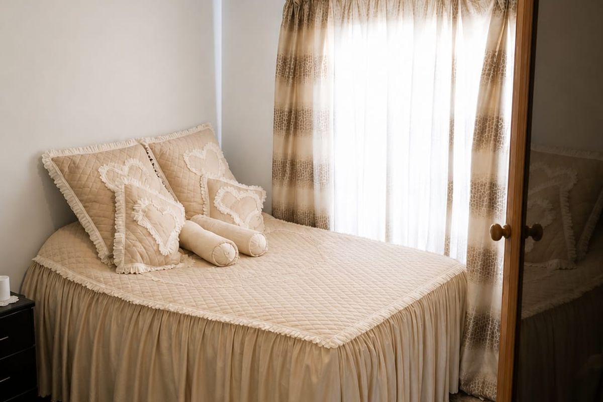A cozy bedroom featuring dark herringbone flooring, neutral wall finishes, and a window dressed with curtains, providing a comfortable and well-maintained living space.