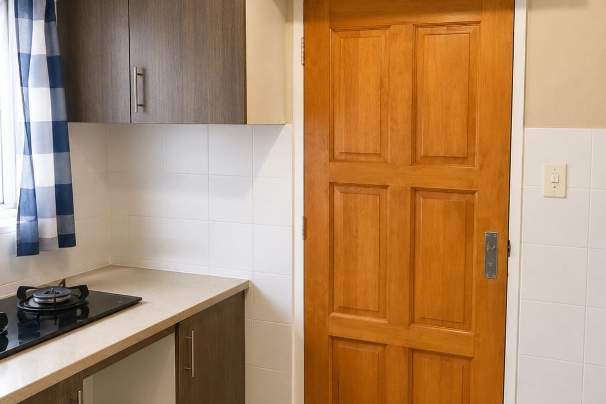 A compact kitchen area featuring built-in cabinetry, a gas hob, tiled splashbacks, and neutral floor tiles, offering a functional and clean workspace.