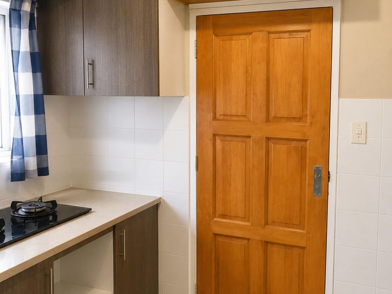 A compact kitchen area featuring built-in cabinetry, a gas hob, tiled splashbacks, and neutral floor tiles, offering a functional and clean workspace.