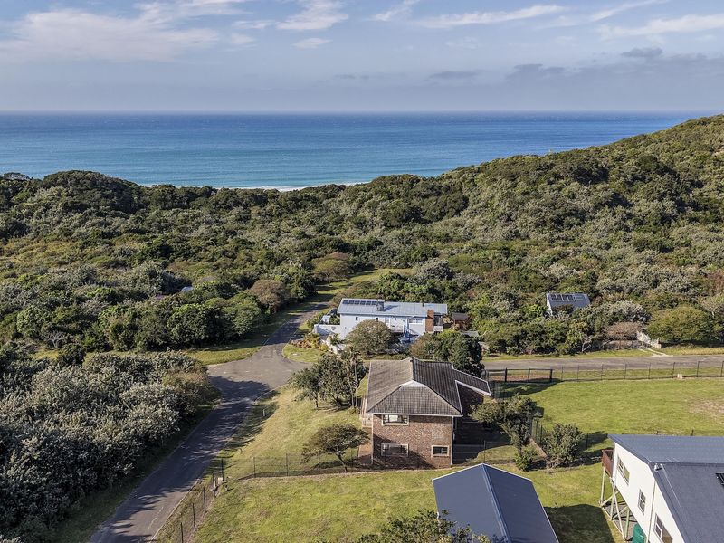 Aerial view of a coastal residential property featuring a tiled roof house, solar panels, and surrounding natural vegetation with ocean views.