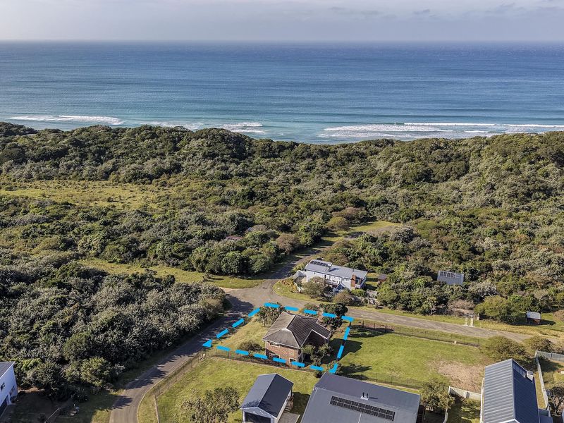 Aerial view of a coastal residential property featuring a pitched roof home, fenced perimeter, and surrounding natural vegetation near the ocean.