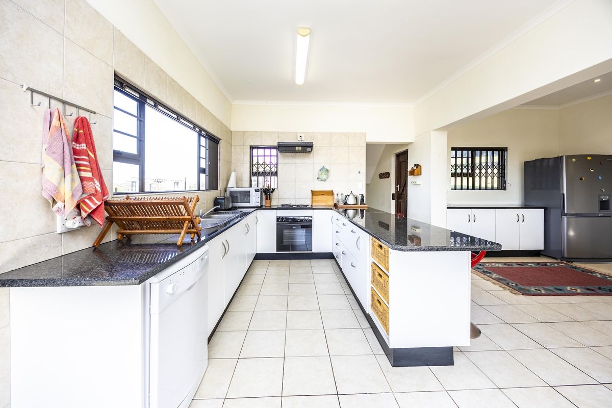 A functional kitchen featuring granite countertops, white cabinetry, built-in oven, hob, and tiled flooring, with an open-plan layout connecting to the adjacent living area.