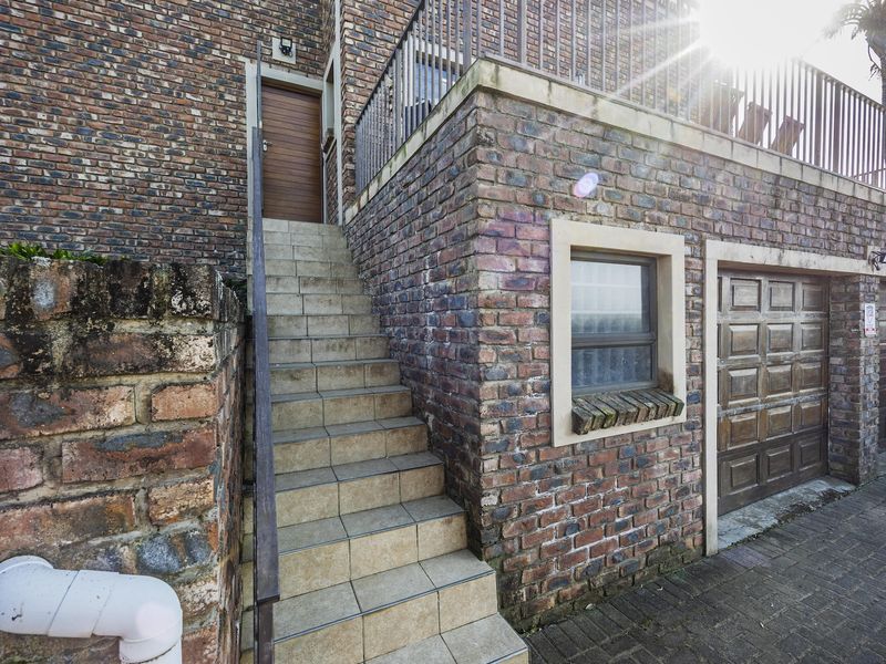 Exterior view of a face brick house featuring a double garage, external staircase leading to an upper level, and paved driveway area.