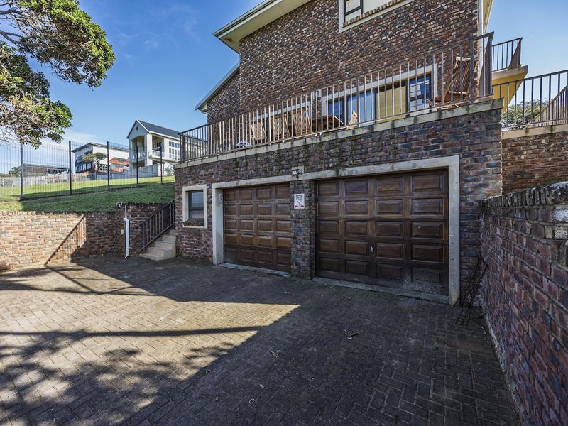 Exterior view of a double garage with a paved driveway, brick facade, and an upper-level balcony with metal railings.