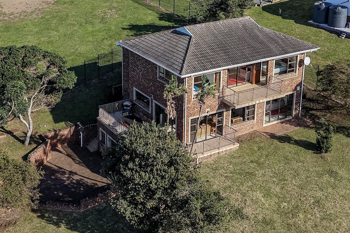 Aerial view of a two-story brick house featuring multiple balconies, a patio area, and surrounding garden space.