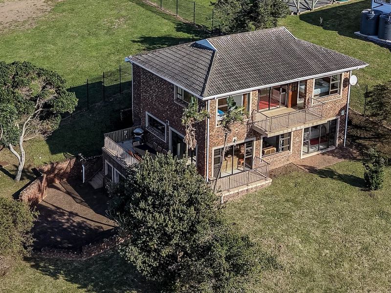 Aerial view of a two-story brick house featuring multiple balconies, a patio area, and surrounding garden space.