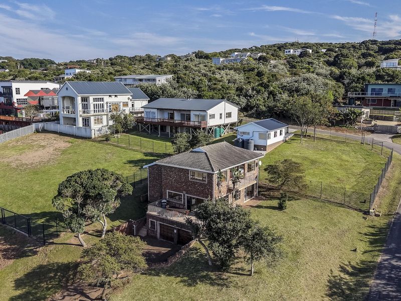 Aerial view of a multi-level brick residential property featuring a spacious yard, fenced perimeter, and paved driveway in a coastal hillside setting.