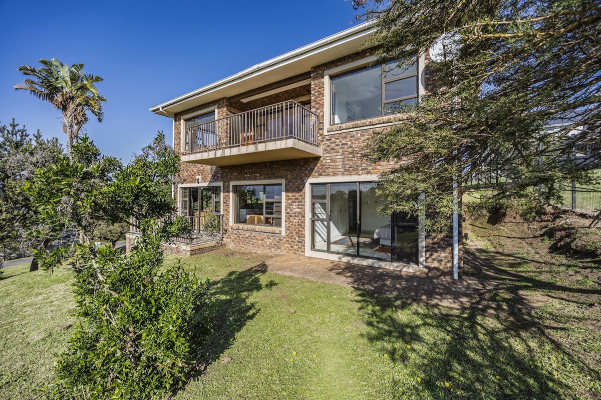 Rear view of a double-story face brick house featuring a balcony, paved patio area, and large sliding glass doors leading to the garden.