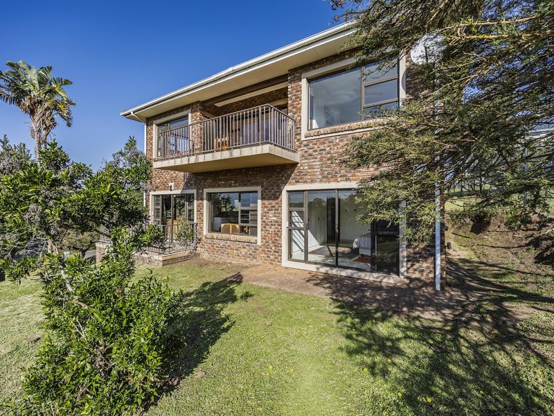 Rear view of a double-story face brick house featuring a balcony, paved patio area, and large sliding glass doors leading to the garden.