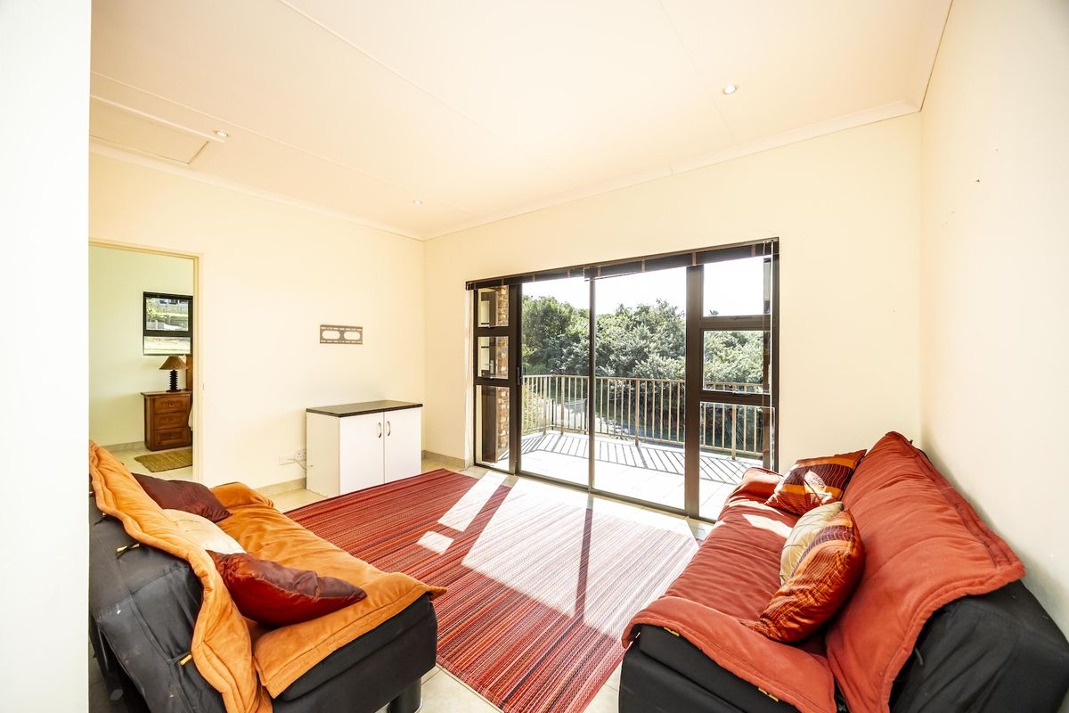 A bright living room featuring tiled floors, recessed lighting, and large sliding glass doors that open onto a balcony with outdoor views.